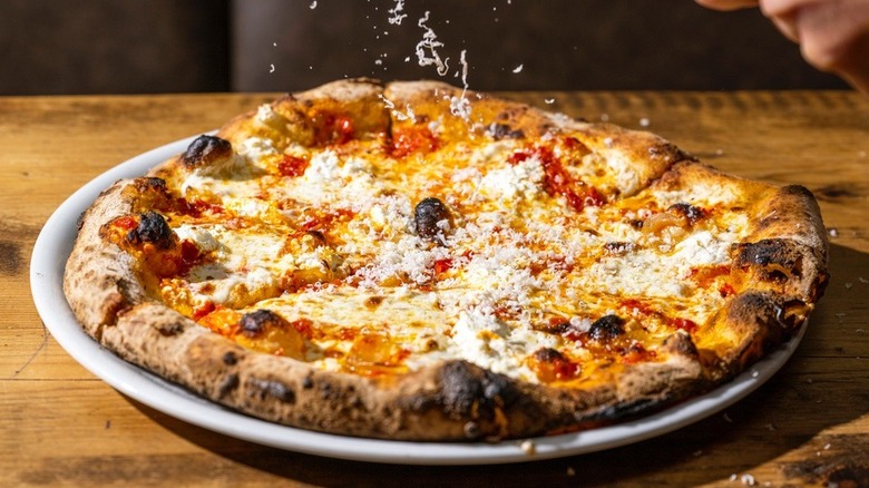 cheese being sprinkled onto pizza pie on wooden table