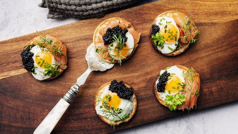 Caviar crackers with salmon and quail eggs on a wooden cutting board