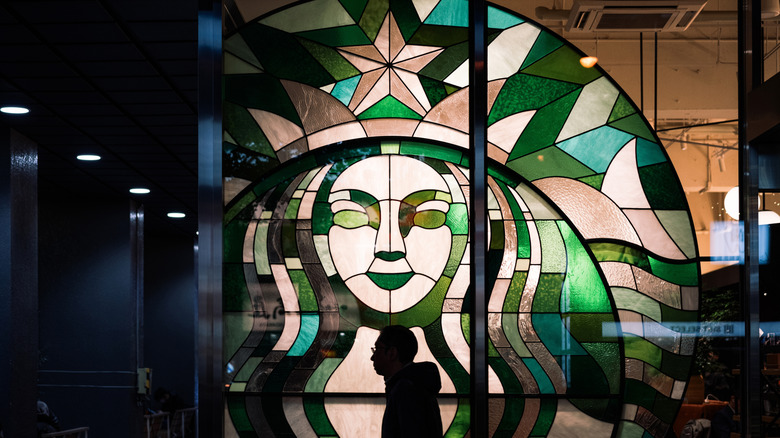 Starbucks interior showing stained glass version of siren logo with silhouette of man walking past