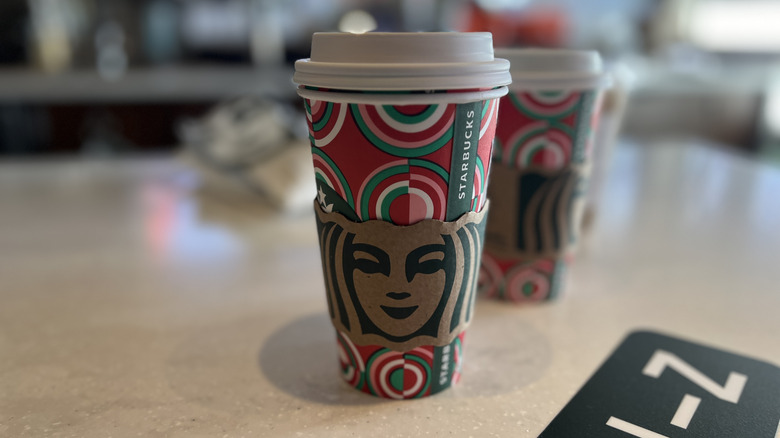 Starbucks holiday to-go cup on table, with green, pink, white, and red half circles on a red background