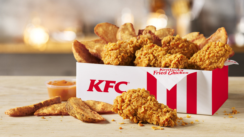 KFC's hot & spicy wings and potato wedges spilling out of a KFC box with dipping sauce on the side