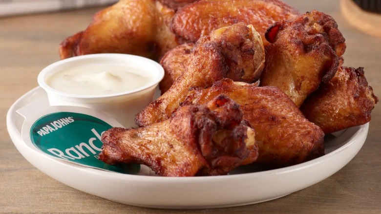 Papa Johns Traditional Style Wings on white plate with a cup of ranch dressing on side