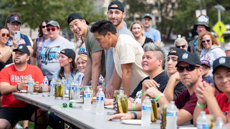 People sit and stand at a table with pickle jars and water bottles