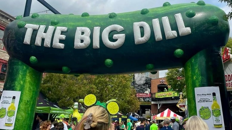People walk under a giant pickle with the words the big dill