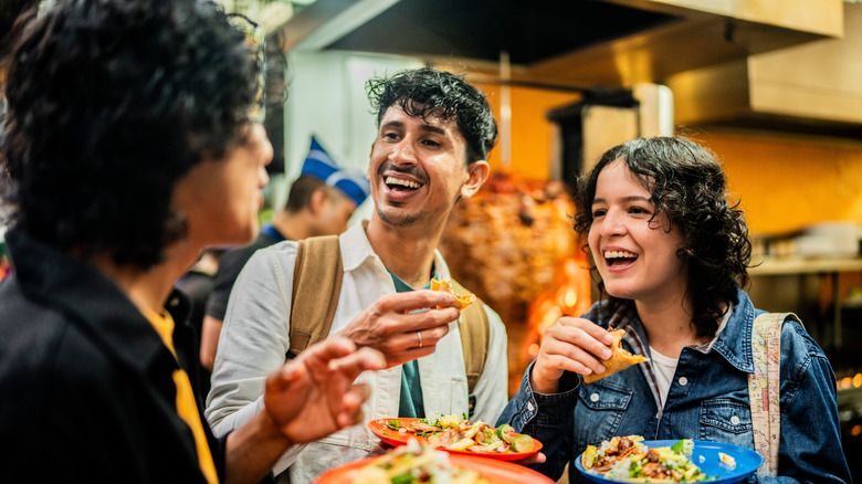 People laughing and eating tacos al pastor in Mexico City.