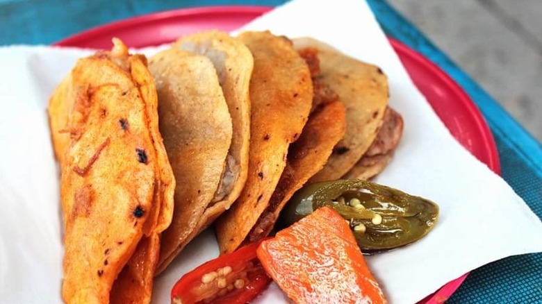 Tacos de canasta lying on a plate with pickles.