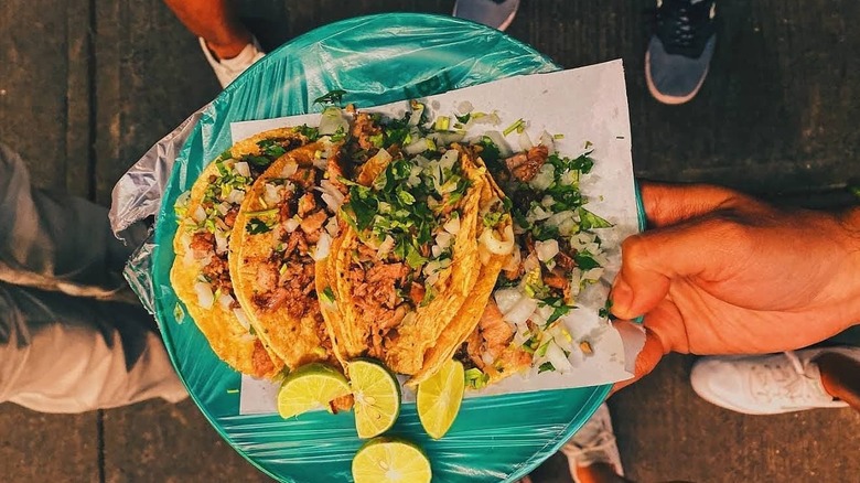 Person holding plate of tacos de suadero with lime.