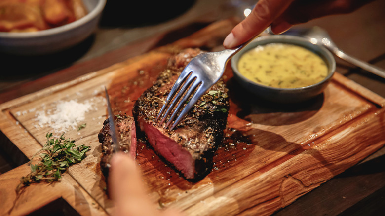 Person cutting a steak with a fork and knife