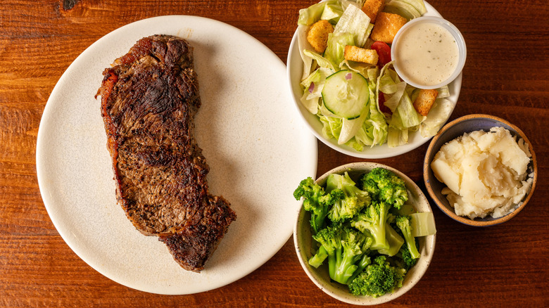 A sirloin steak with a salad, mashed potatoes, and broccoli