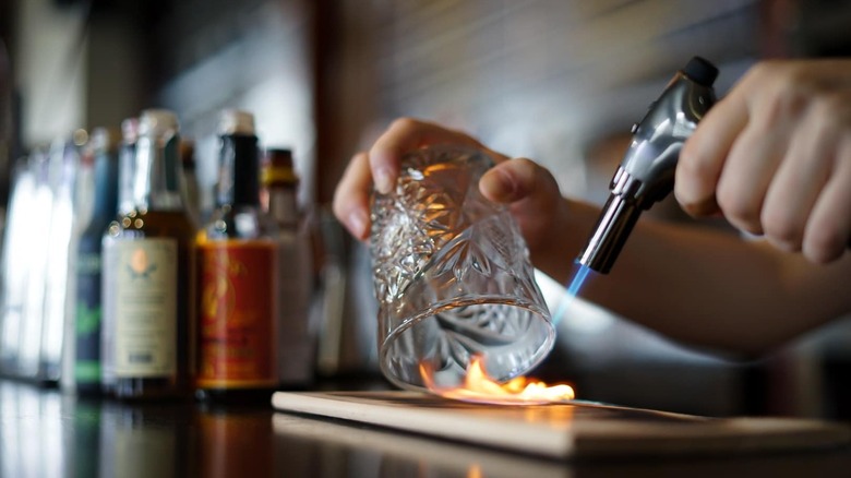 Bartender using blowtorch on whiskey glass
