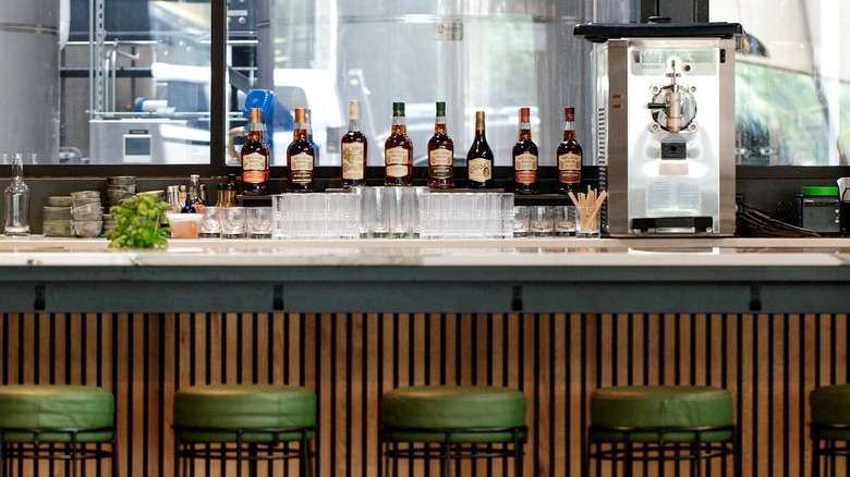 Marble bar with green barstools overlooking selection of whiskey bottles