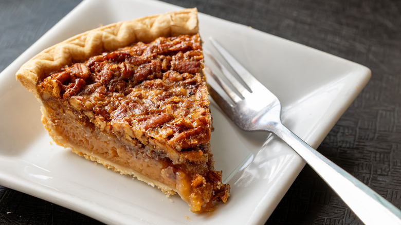 A slice of pecan pie on a white square plate with a fork