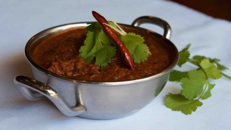 A copper dish of Phall, the world's spiciest curry, garnished with herbs and a chili pepper at Brick Lane Curry House