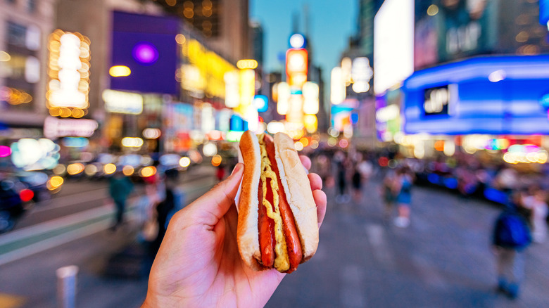 person holding hotdog with blurred street in background