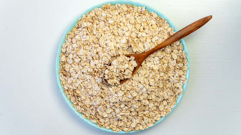 A wooden spoon scoops from a bowl of uncooked oats