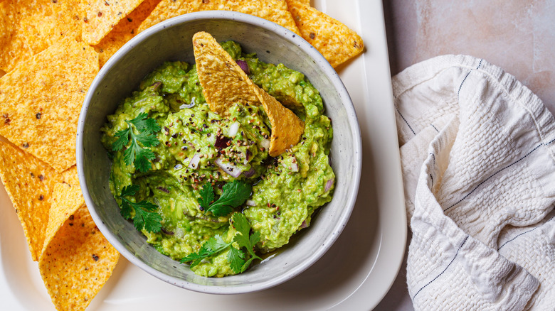 Bowl of guacamole garnished with cilantro on plate with tortilla chips