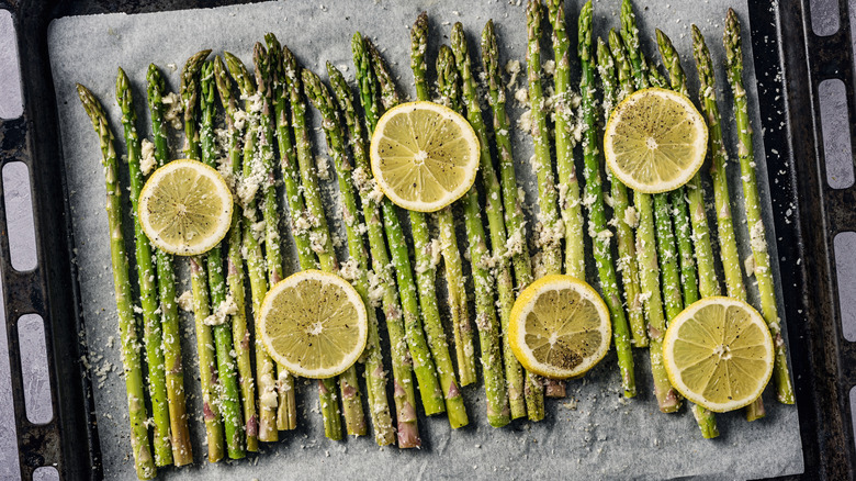 Roasted asparagus with lemon slices laid out on parchment paper