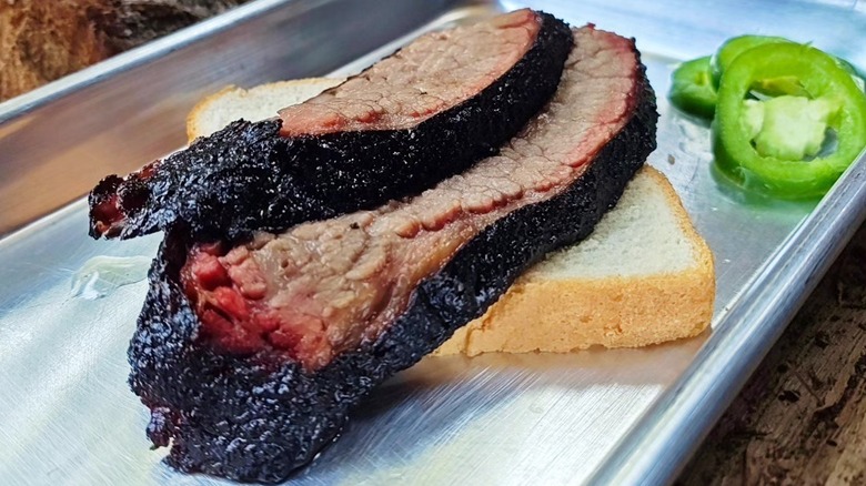 A close-up of two slices of brisket on white bread in a metal tray