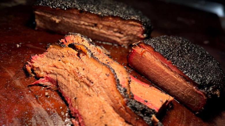 A brisket cut in half with several slices stacked in front. Gorgeous dark bark and deep smoke ring.