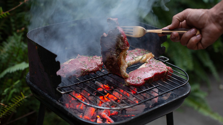 hand flipping steak on charcoal grill