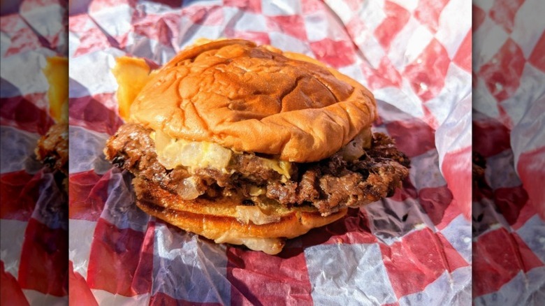 Close-up of a 7th Street Burger cheeseburger on its red-and-white checkered paper
