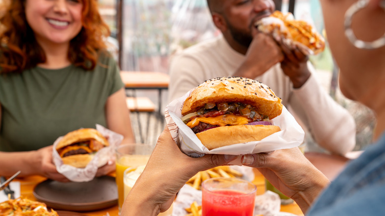 Three people smiling and eating cheeseburgers