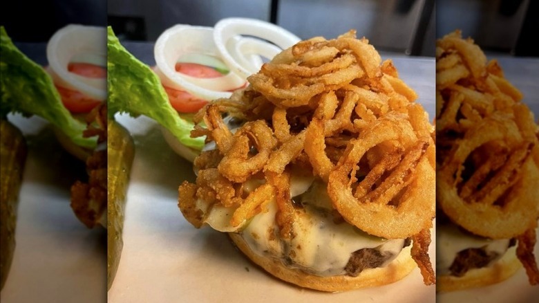 Burger with onion strings, open with tomato, onion, and lettuce on top bun