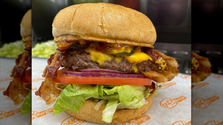 An Only Burger deluxe burger piled high with toppings on an Only Burger-labeled napkin