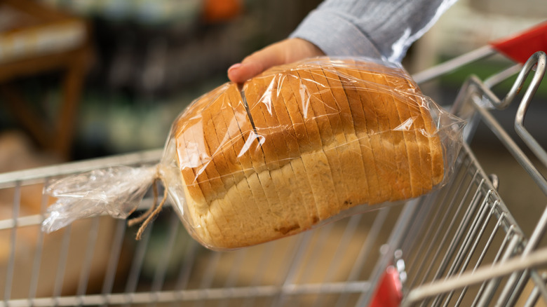 Putting packaged bread into shopping cart at store.