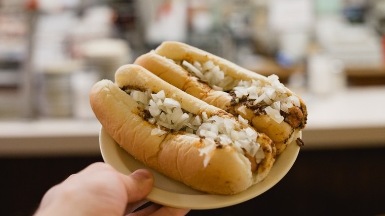 A hand holding up a plate of two chili dogs