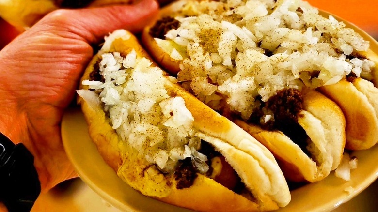 A hand holding a plate of three hot dogs