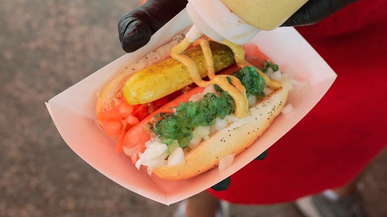 A Chicago dog with mustard being poured onto it