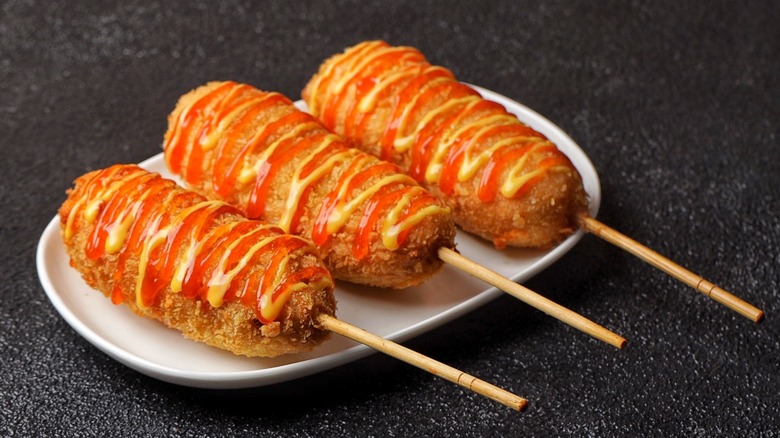 Three Korean corn dogs topped with ketchup and mustard on a white plate