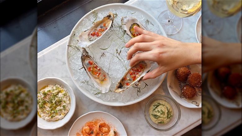 Person picking up on oyster from a round plate of oysters on ice