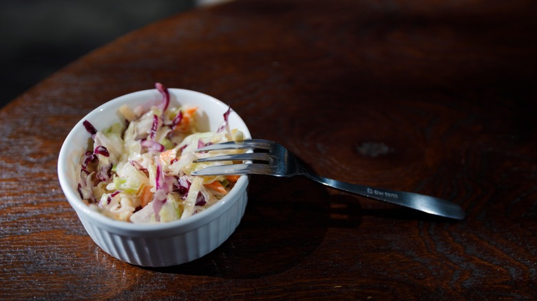 A ramekin of coleslaw with a fork propped up on the rim.