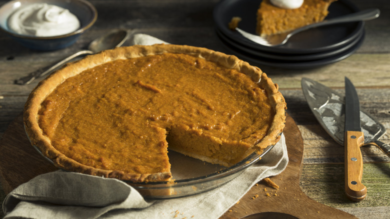 An already sliced sweet potato pie placed on a round dish, resting on a white towel atop a wooden board