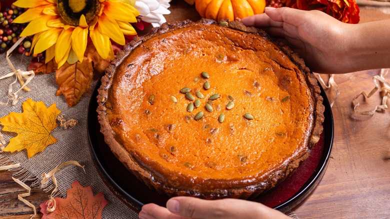 Hands putting a pumpkin pie on a table
