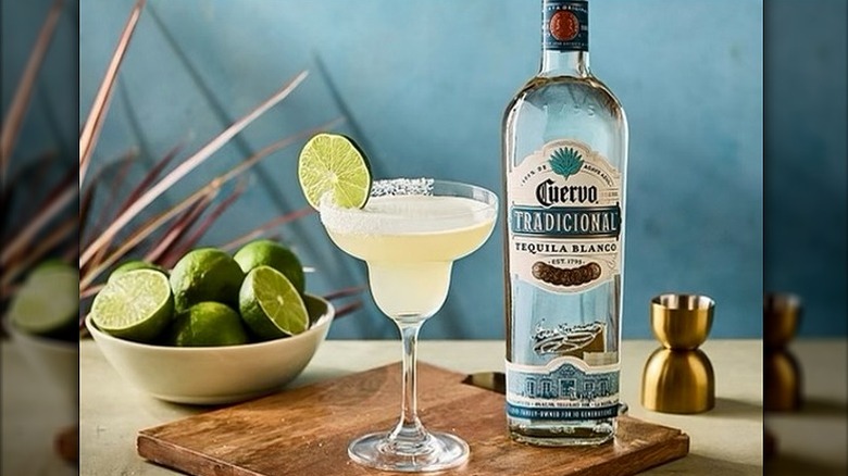 Bottle of Jose Cuervo Tradicional Tequila Blanco with a margarita and lime slice on cutting board with a bowl of limes