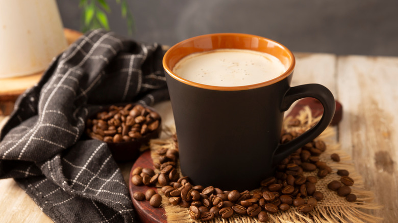 Cup of coffee sitting on a table with coffee beans