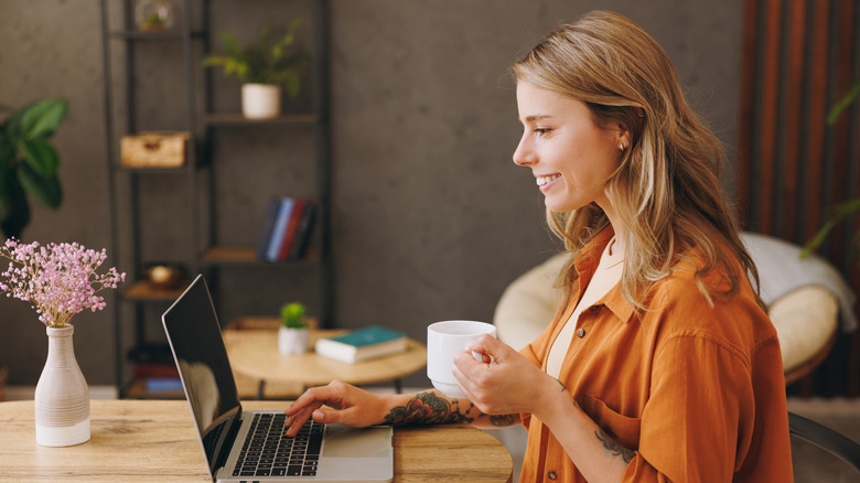 Woman drinking coffee while typing on laptop.