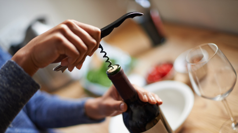 Person opening a wine bottle with a corkscrew