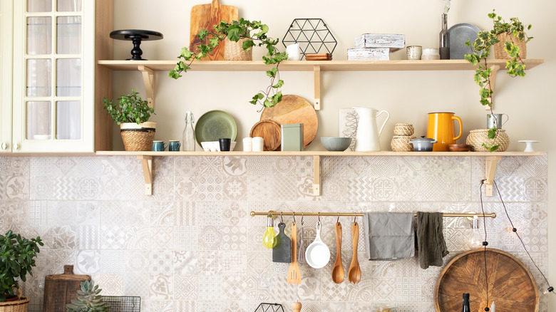 A kitchen's open shelves are dynamicly styled with wooden boxes, glass pitchers, tin boxes, plants, and more.