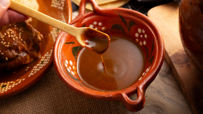 closeup of mole sauce in a red bowl being stirred with a wooden spoon