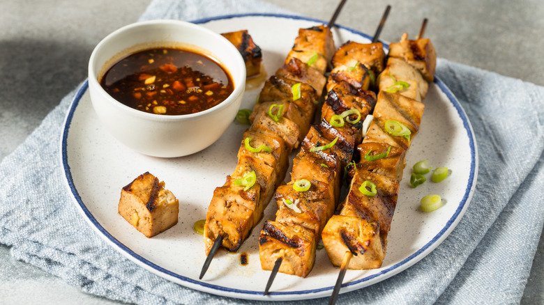 Barbecued tofu skewers on a plate with dipping sauce