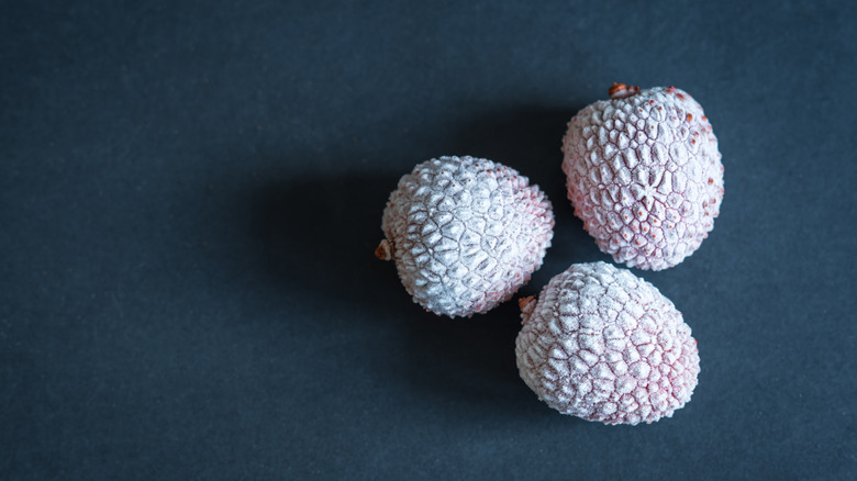 Three frosty, frozen lychees with peels on, on a dark blue background