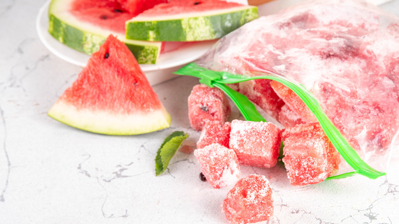 An open zippered plastic bag with frozen watermelon cubes next to watermelon slices
