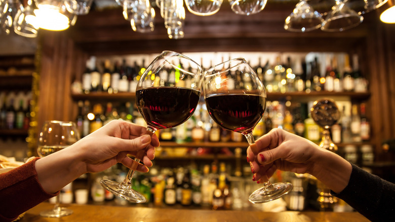 Two hands clinking together wine glasses full of red wine