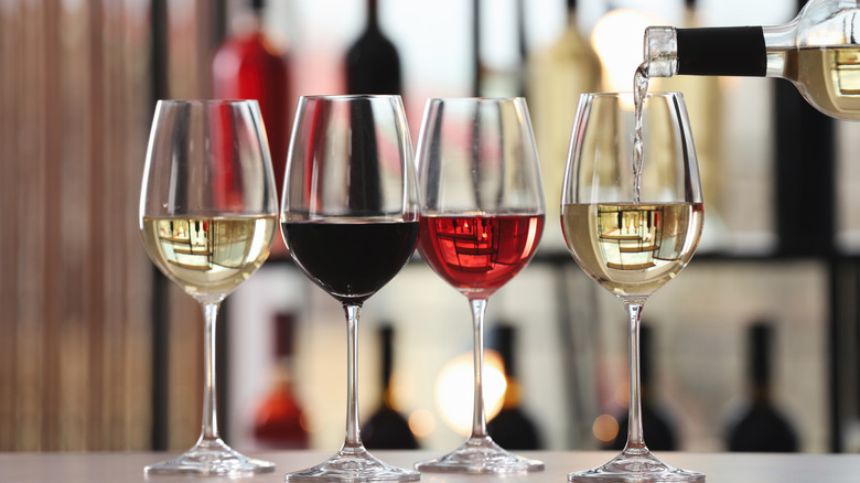 Four wine glasses on counter half full of white, red, and rose wine.