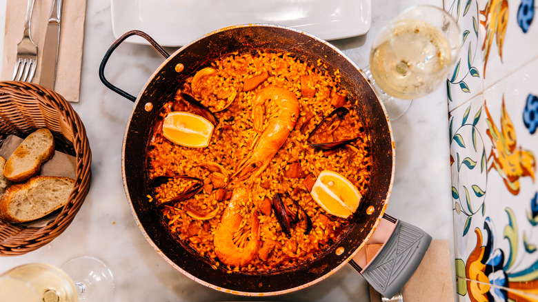Seafood paella in a pot next to glasses of white wine