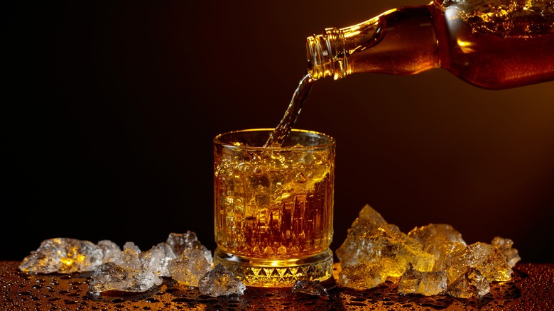 Whiskey poured from a bottle into a glass surrounded by ice